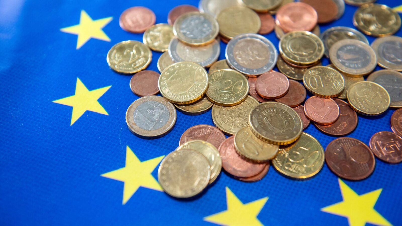 Euro-Münzen auf blauem Untergrund mit gelben Sternen als Symbol für Geldanlage