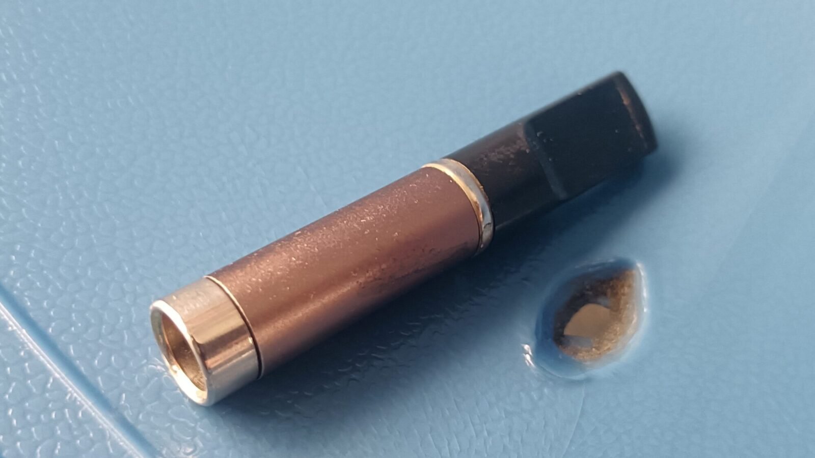 Einweg-E-Zigarette mit kupferfarbenem Gehäuse liegt auf einer blauen Fläche