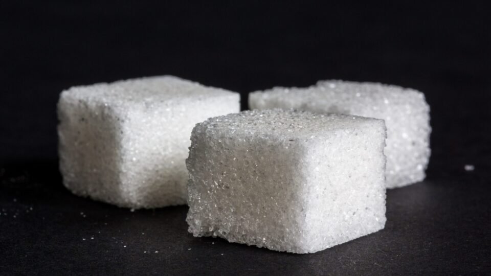 Drei weiße Zuckerwürfel liegen nebeneinander vor dunklem Hintergrund in Nahaufnahme