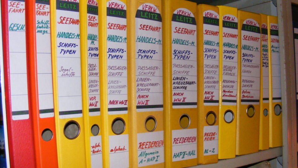 Bunte Aktenordner stehen dicht nebeneinander in einem Regal eines Büros