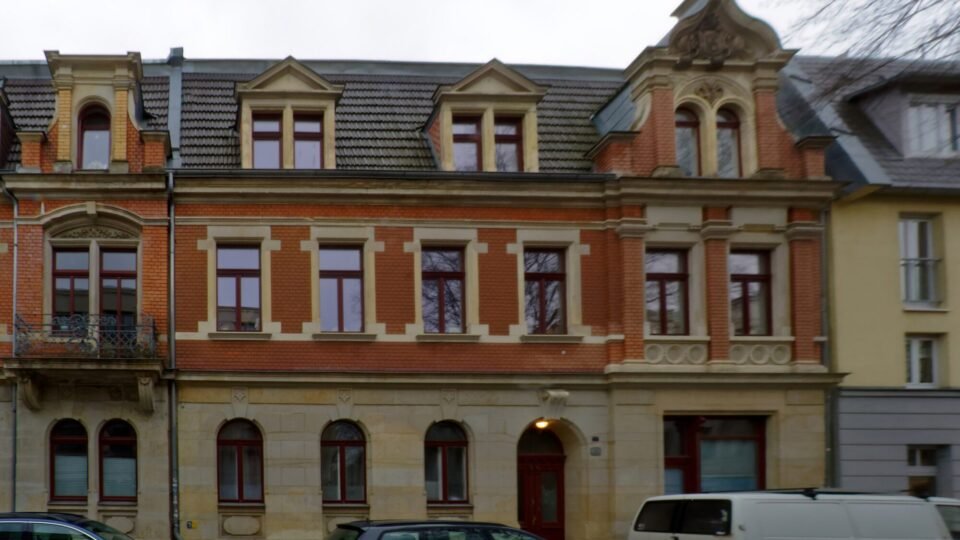 Fassade eines Gründerzeit-Mehrfamilienhauses mit geparkten Autos vor dem Eingang