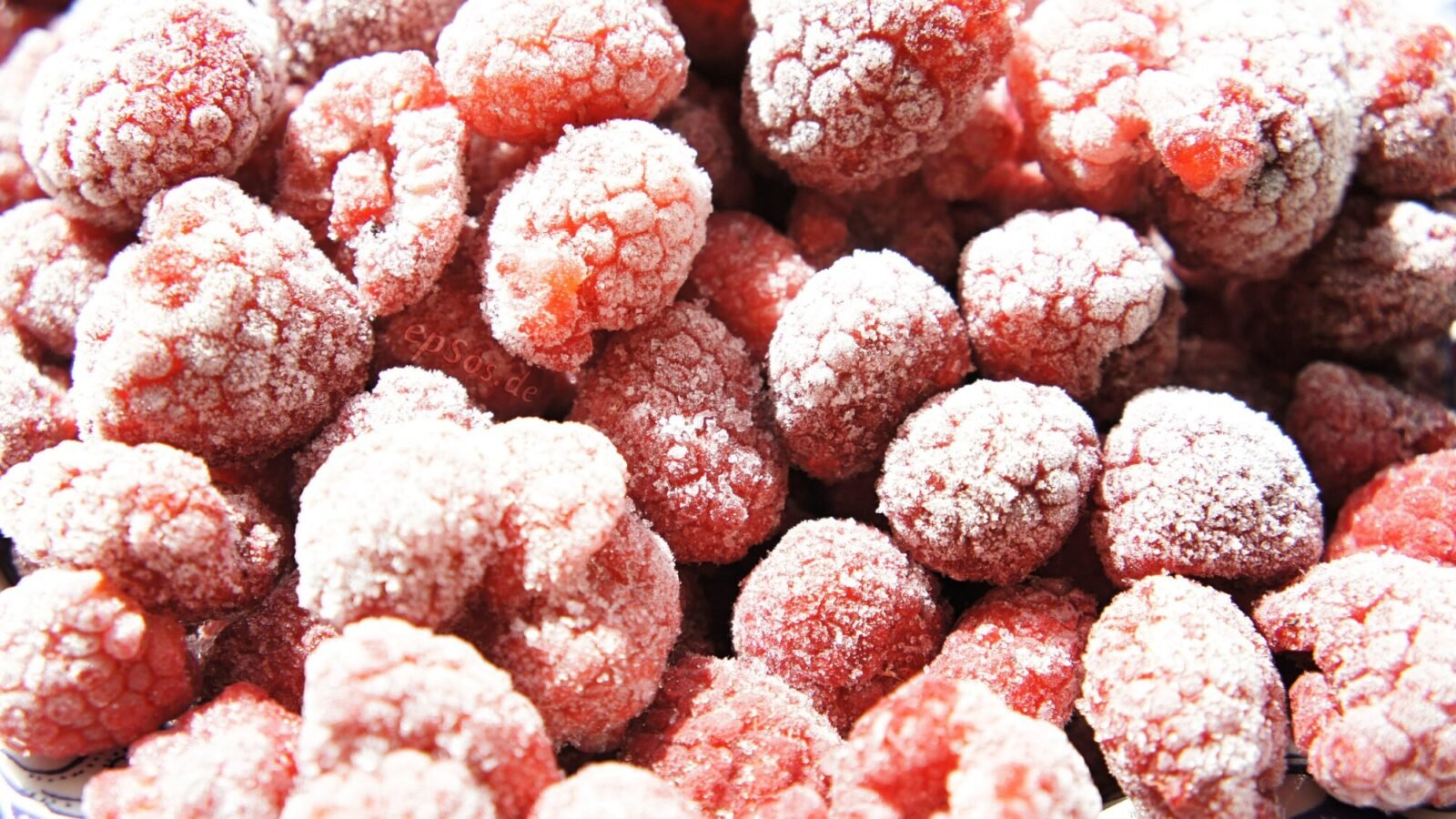 Gefrorene Himbeeren mit Eiskristallen dicht nebeneinander in einer Nahaufnahme