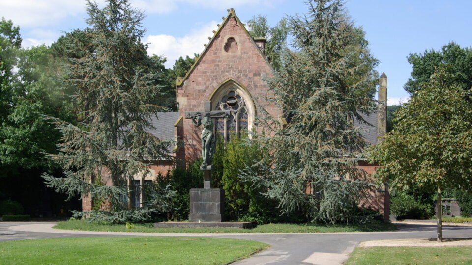 Backsteinkapelle auf dem Trierer Hauptfriedhof zwischen Bäumen und Rasenflächen